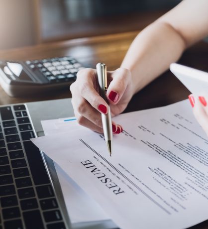 woman holding pen over resume application with smart phone and using computer laptop to job search on online internet. applying for a job concept.